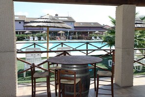 A poolside area with a round wooden table and chairs, a large barrel, and a view of a building with a sign reading "LE CANTINE". - Appartamento Palazzeta With Pool, Near the Sea (Cecina)