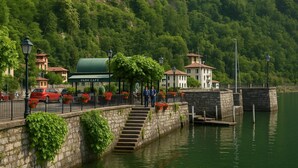 Un puente de piedra que lleva a un café en un parque, con mesas al aire libre y vistas a un lago.