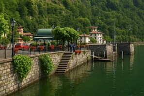 Un pont de pierre menant à un café situé dans un parc, avec une terrasse et une vue sur un lac.