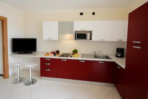 A modern kitchen with white and red cabinets, a microwave, a sink, and a television.