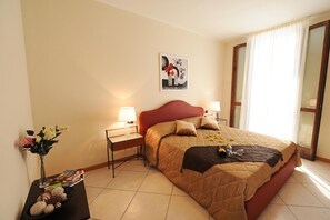 Ein Hotelzimmer mit einem Bett, zwei Nachttischen, einem Wandbild und einem Fenster mit Vorhängen.