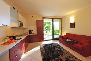 A modern kitchen with a microwave, sink, and red cabinets. There is a red sofa and a black rug in the living area. - Residence Eden Azalea 2, Argegno, Italy (Argegno)