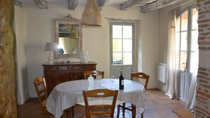 Uma sala de jantar com uma mesa redonda, cadeiras de madeira, um candelabro, um espelho e uma janela com cortinas.