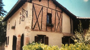 Uma casa tradicional em enxaimel com um telhado pontiagudo, uma pequena janela com uma caixa de flores e um candeeiro na parede.