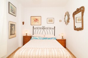 Un dormitorio ordenado con cama, dos mesitas de noche y una obra de arte colgada en la pared.