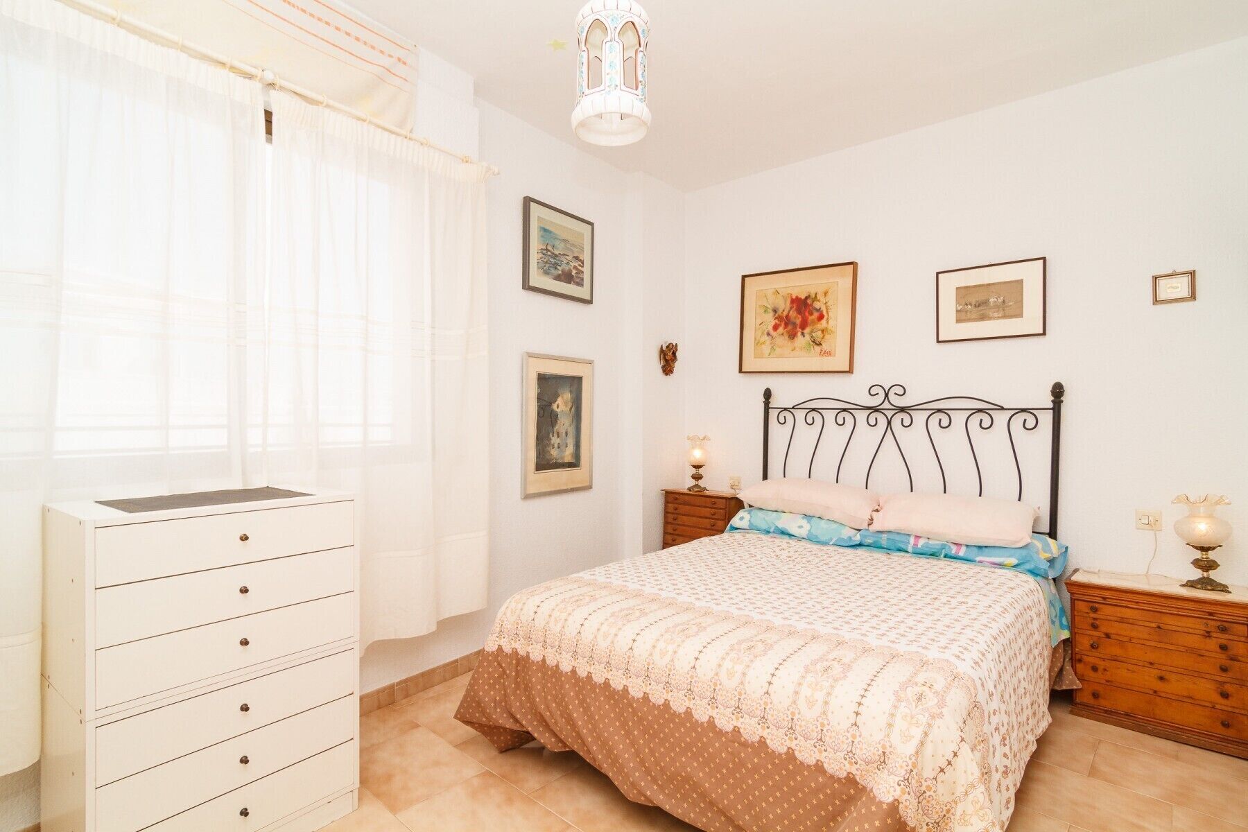 Une chambre à coucher avec un lit, une commode, une table de chevet et une lampe.