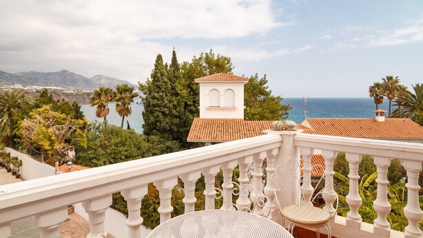 A balcony with a white balustrade, a round table, and a chair. In the background, there is a view of the sea and a mountainous landscape. - Carabeillo 13 Apartments by Casasol (Nerja)