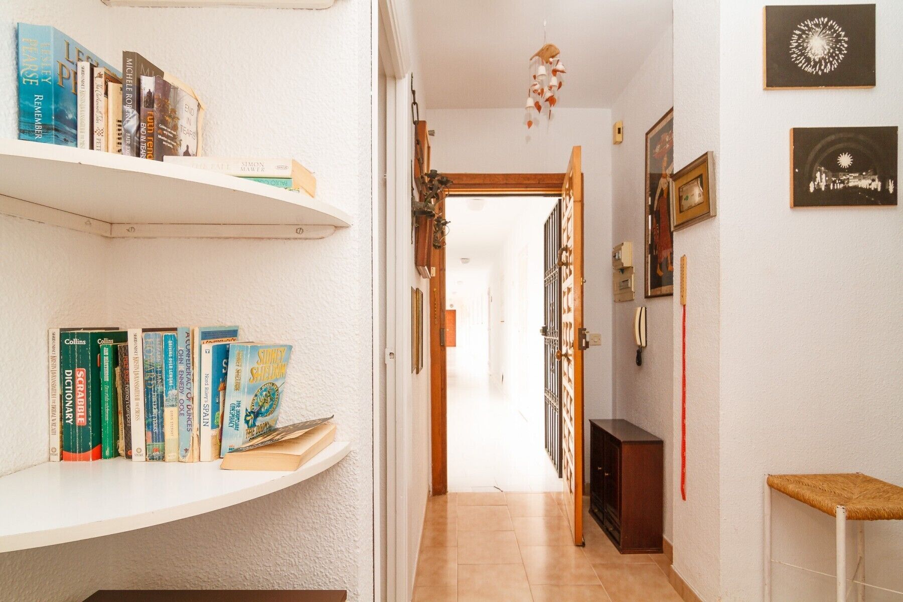 A hallway with bookshelves on both sides, a wooden door at the end, and a small table with a basket on the right.
