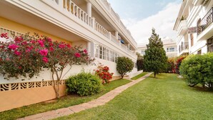 A well-maintained courtyard with a paved pathway, neatly trimmed grass, and various shrubs and flowering plants. - Carabeillo 13 Apartments by Casasol (Nerja)