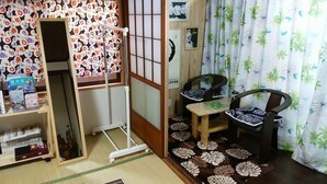 Ett traditionellt japanskt rum med tatamimattor på golvet, en shojiskärm, en futonmadrass, ett litet bord med en grön matta och en stol med ett mönstrat sittdyn.