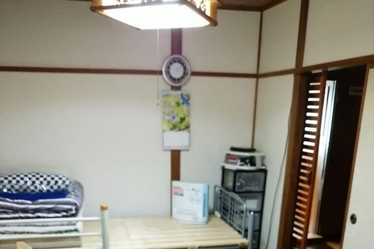 Una habitación con cama, un escritorio pequeño, una silla, un calefactor y una puerta.