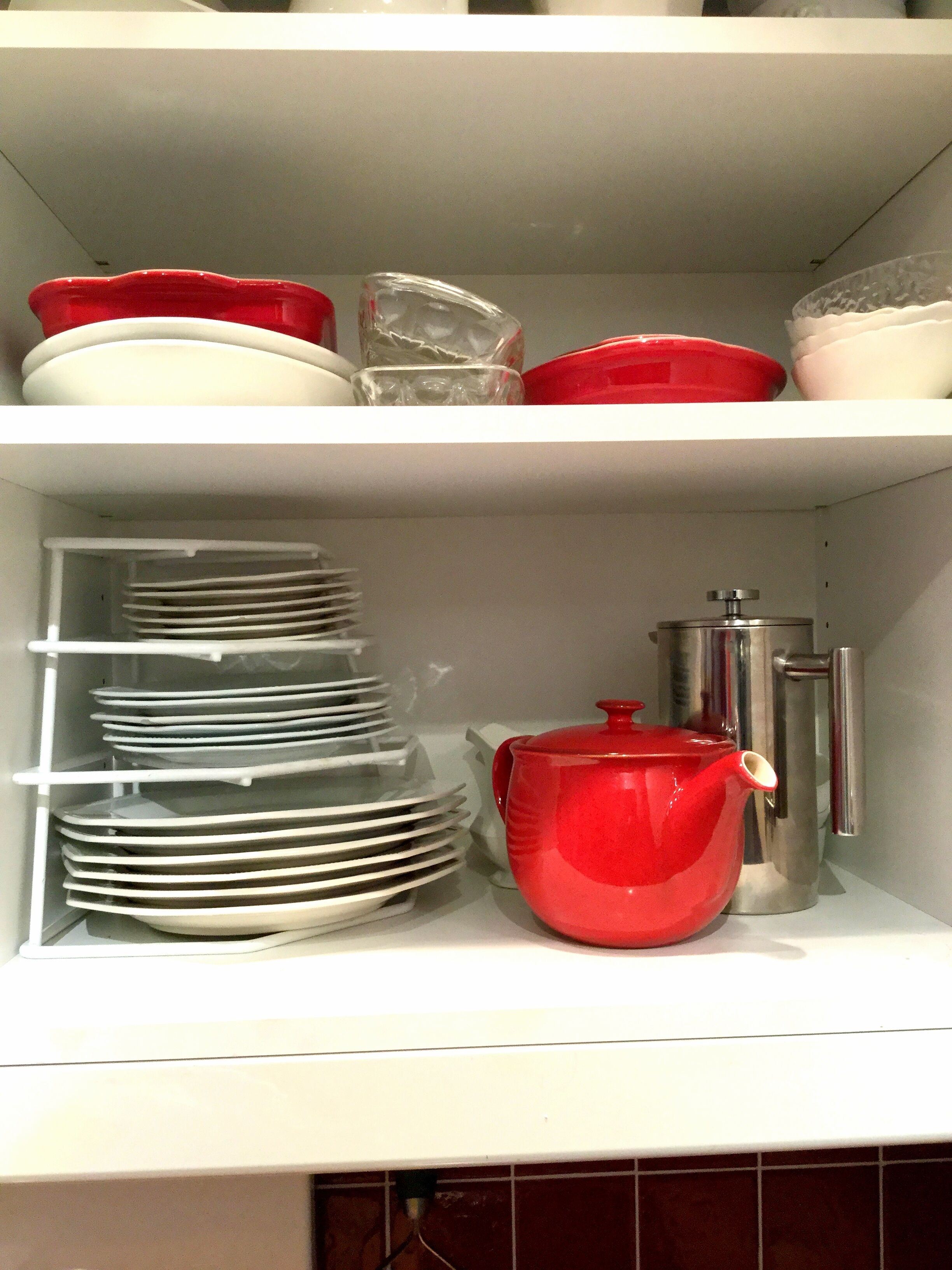 A kitchen shelf with white plates, a red pot, and a stainless steel kettle.