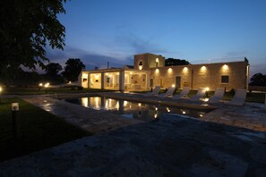 Un espace aménagé au bord de la piscine, avec des chaises longues, et un bâtiment doté de nombreuses fenêtres et d’un balcon.