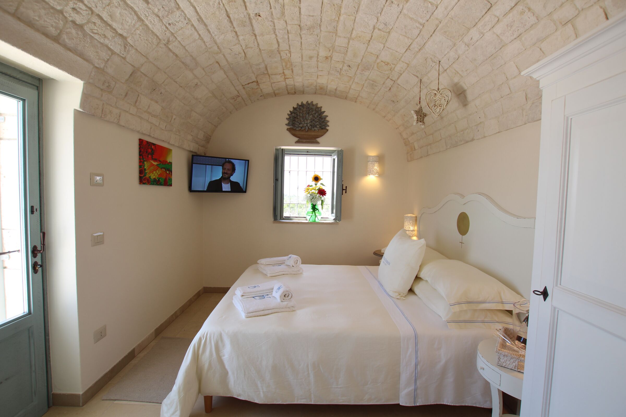 A bedroom with a bed, a television, a window with a flower vase, and a door.