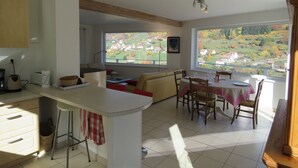 Eine moderne Küche mit Essbereich, große Fenster mit Blick auf ein Dorf und eine gemütliche Sitzecke.