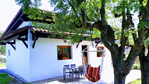 A white building with a tiled roof, a small porch with a chair and table, and a hammock hanging from a tree. - Rural house with garden and terrace between two natural parks. (Igorre)