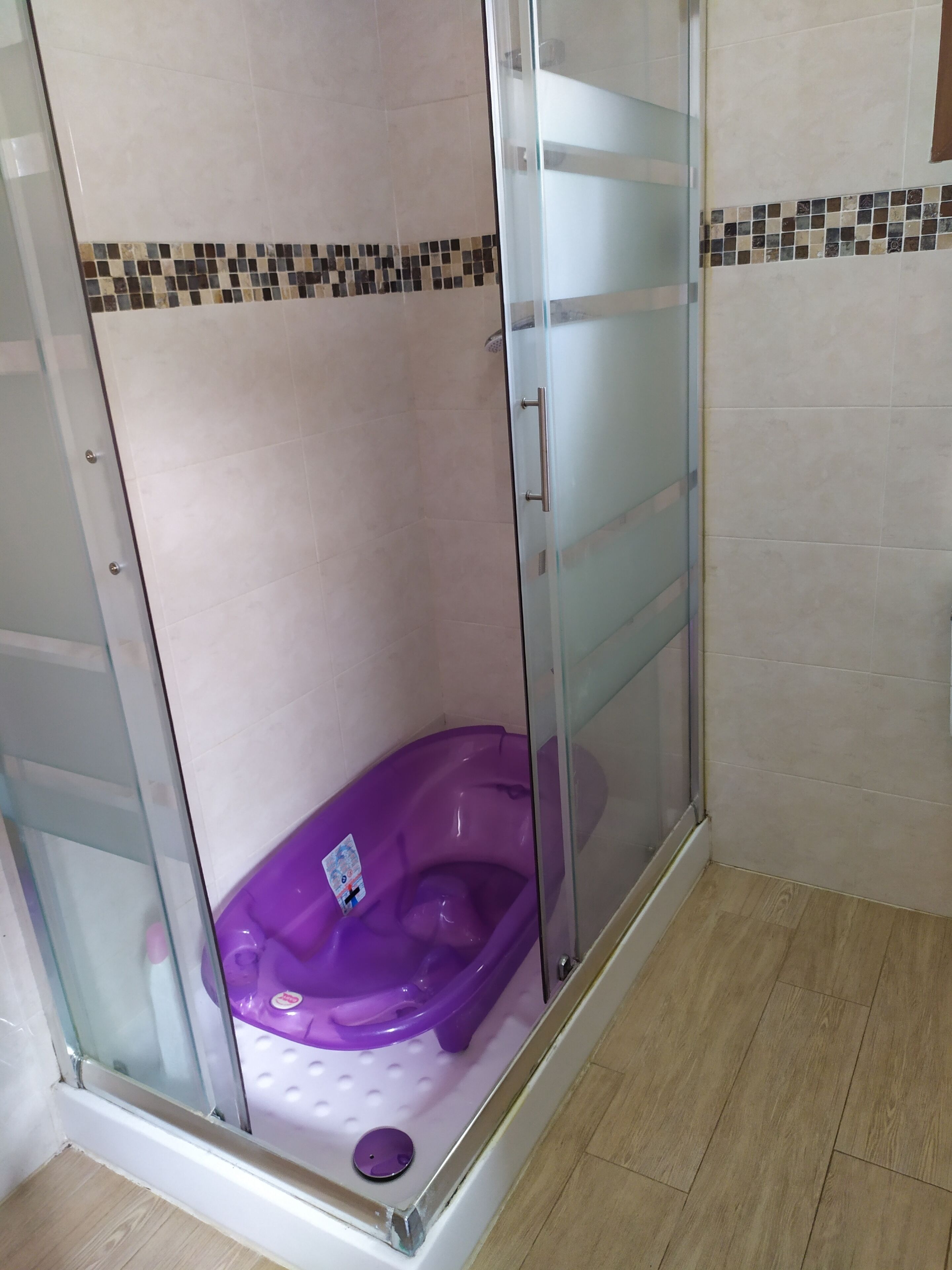 A shower enclosure with a glass door, a purple bathtub, and a tiled floor.