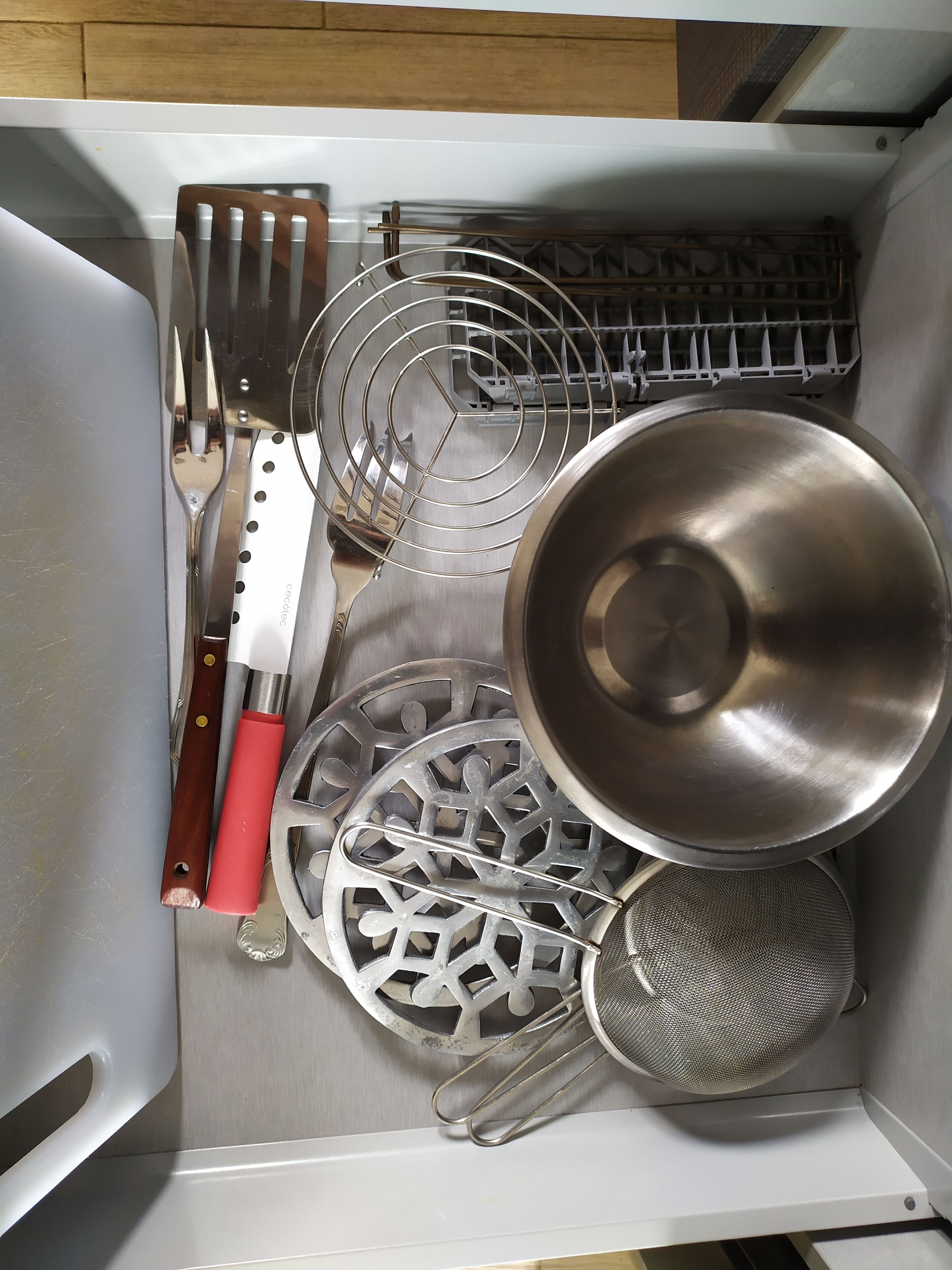 A kitchen drawer with utensils, including a knife, spatula, and strainer.