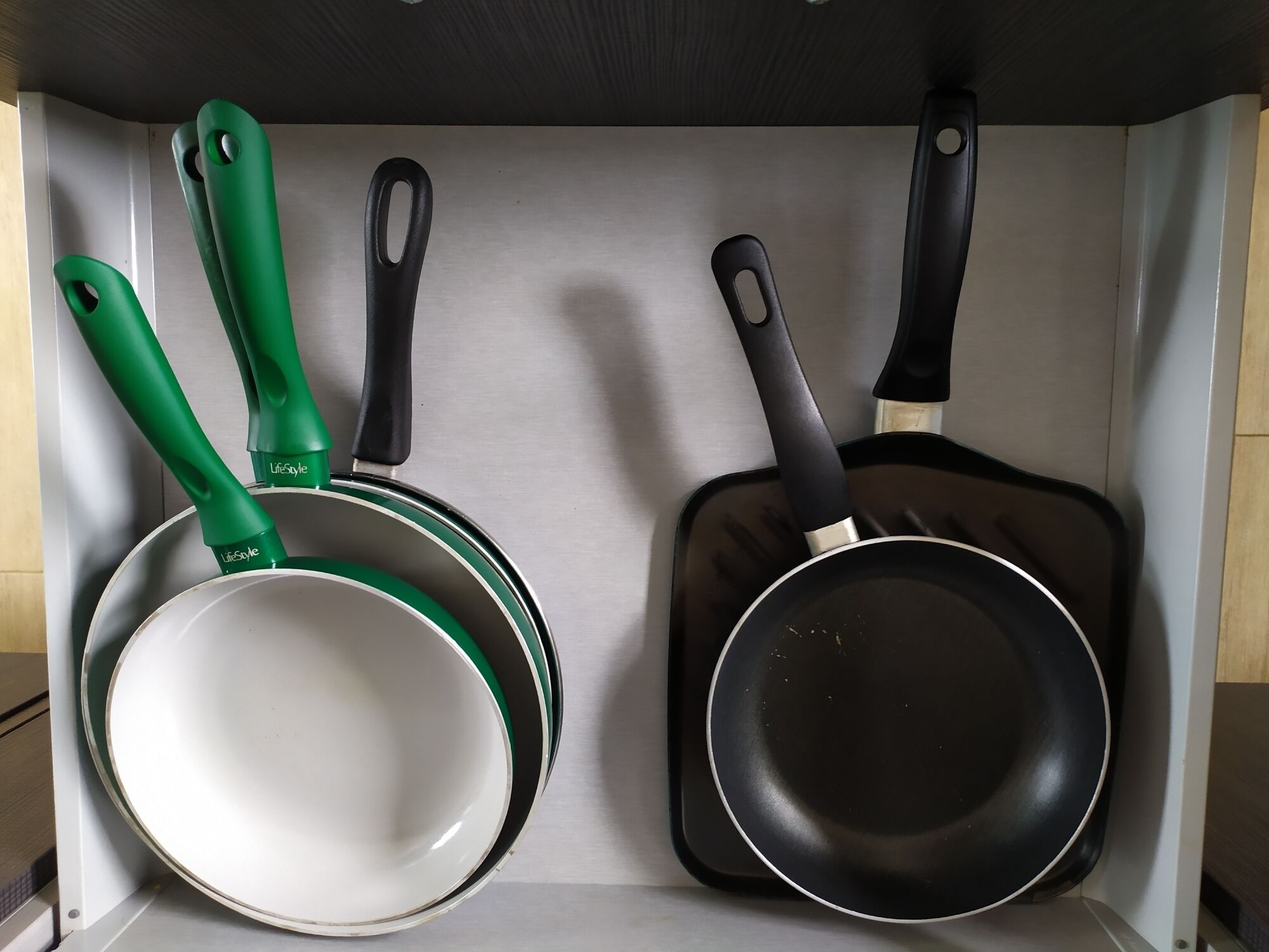 Una cocina con un armario blanco que contiene una sartén blanca, una sartén verde y una sartén negra.