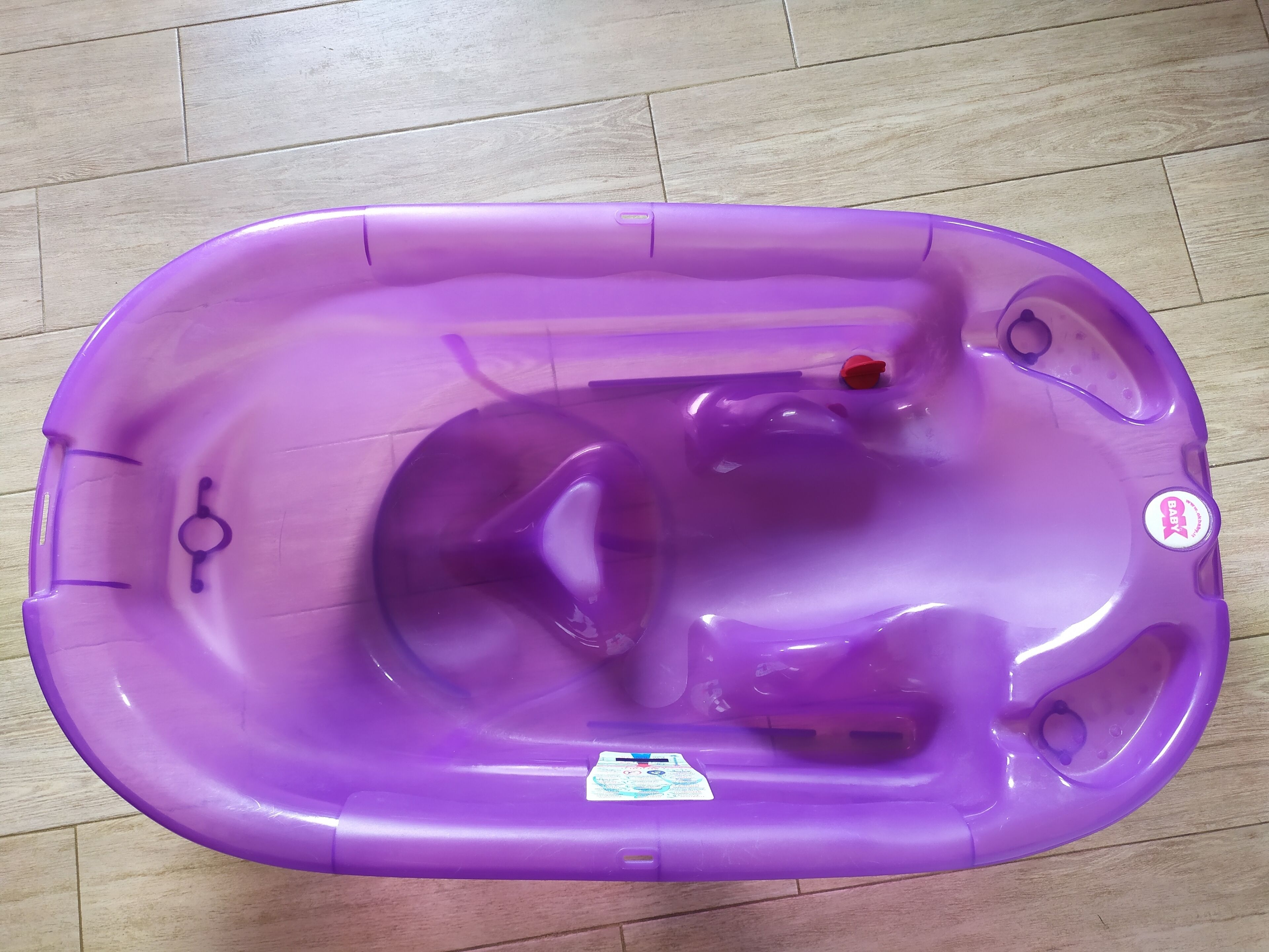 Una bañera morada para bebé con tapa roja, un agujero pequeño y una etiqueta en el lateral.