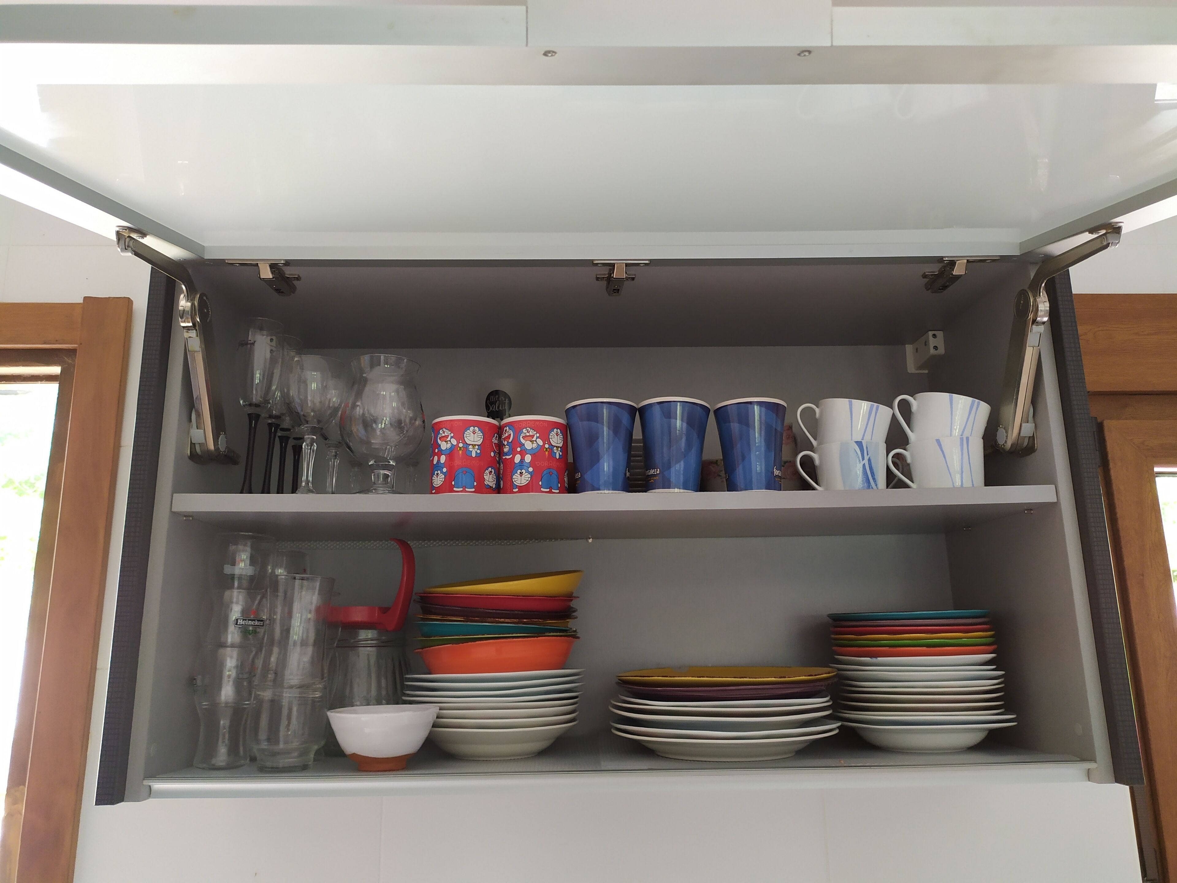 Um armário de cozinha com prateleiras contendo diversos pratos, copos e uma garrafa de água.