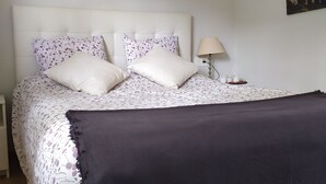 A neatly made bed with floral bedding, a dark throw blanket, and a bedside lamp. - Rural house with garden and terrace between two natural parks. (Igorre)