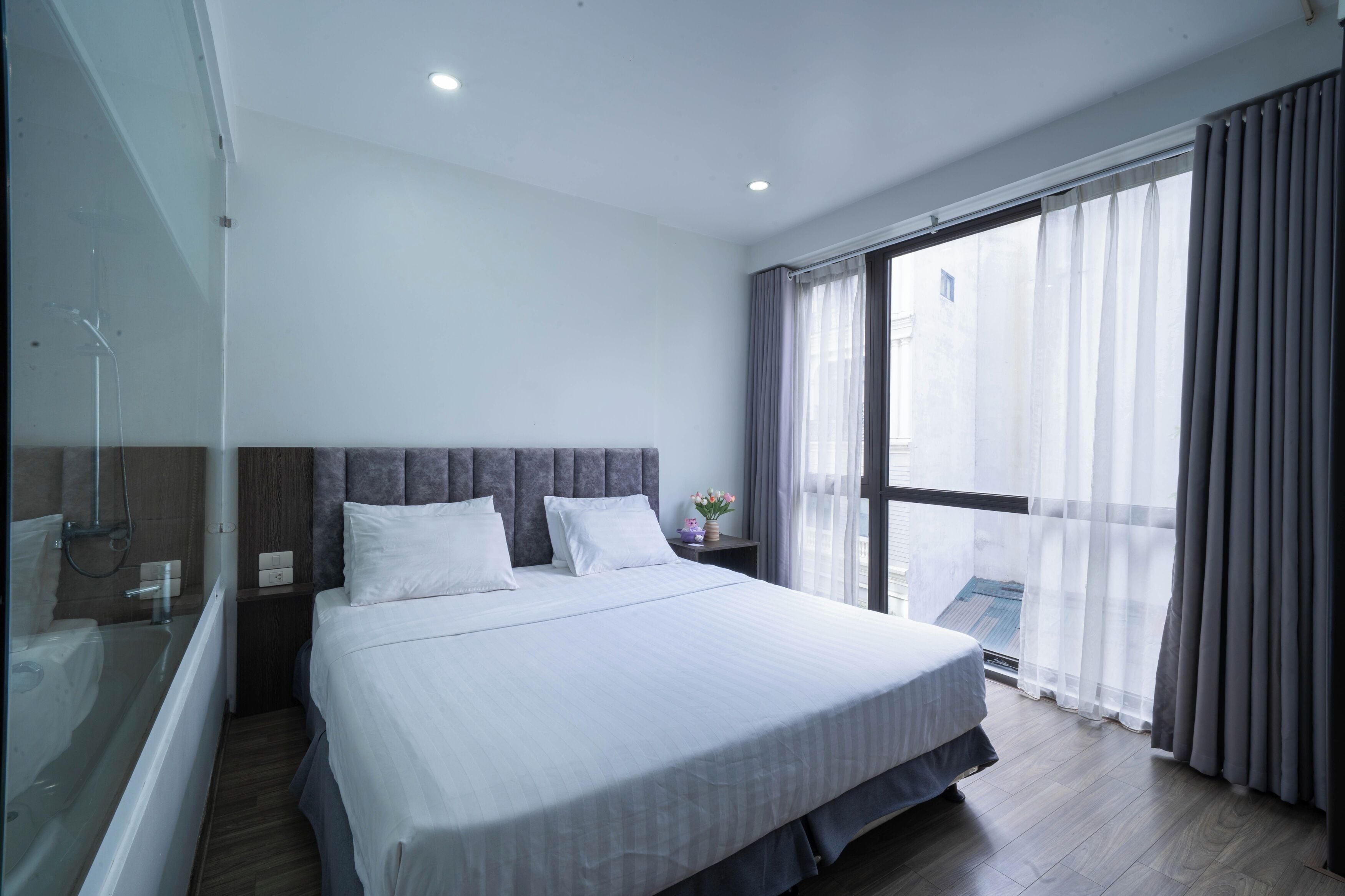 Ein modernes Hotelzimmer mit einem großen Bett, einer Duschkabine aus Glas und einem Balkon mit Vorhängen.