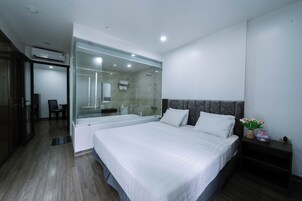 Una habitación de hotel moderna con una cama grande, cabina de ducha de vidrio, piso de madera oscura y un pequeño rincón de descanso.