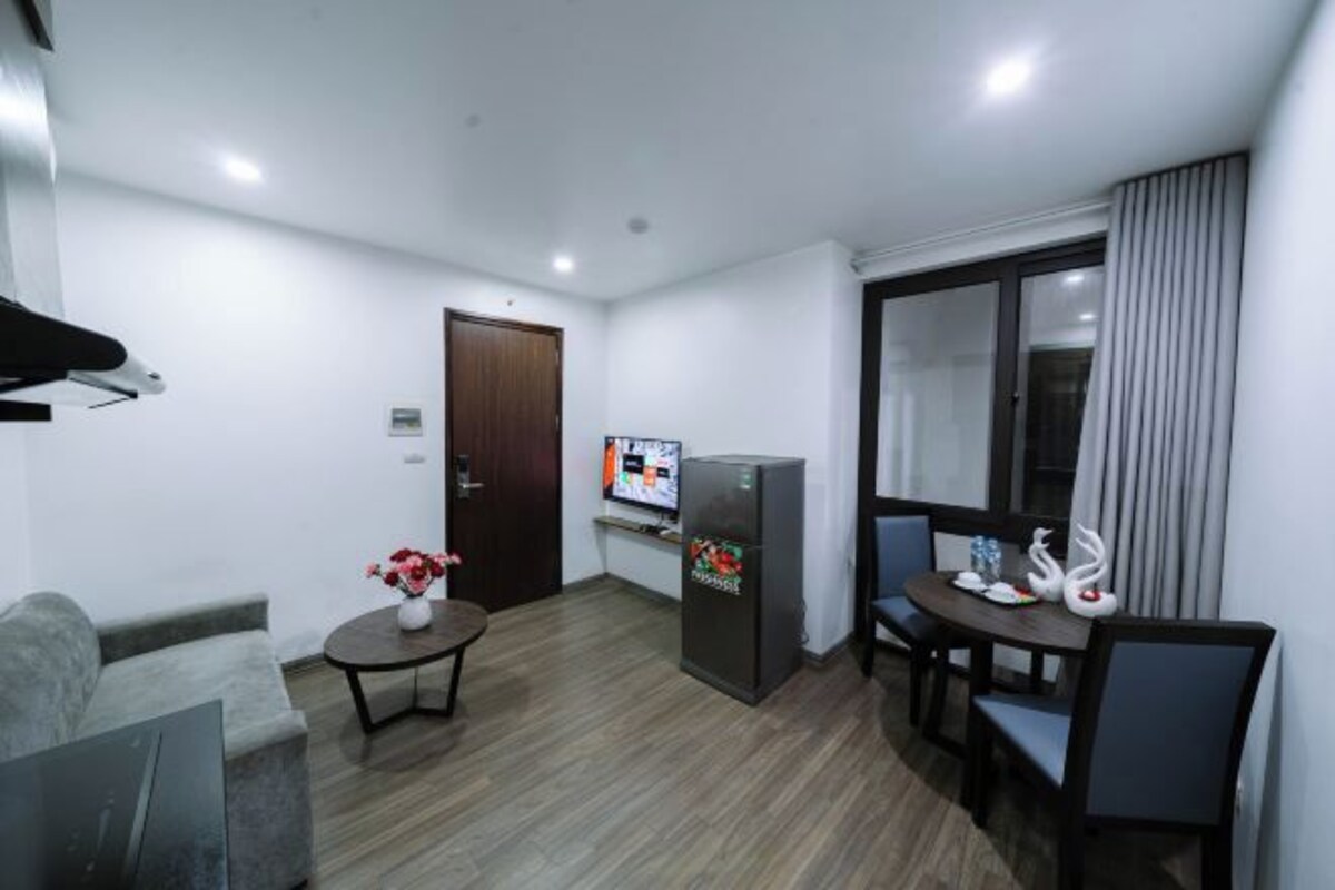 Una sala de estar moderna con un sofá, una mesita con un florero, una zona de comedor con sillas, un refrigerador y un televisor.