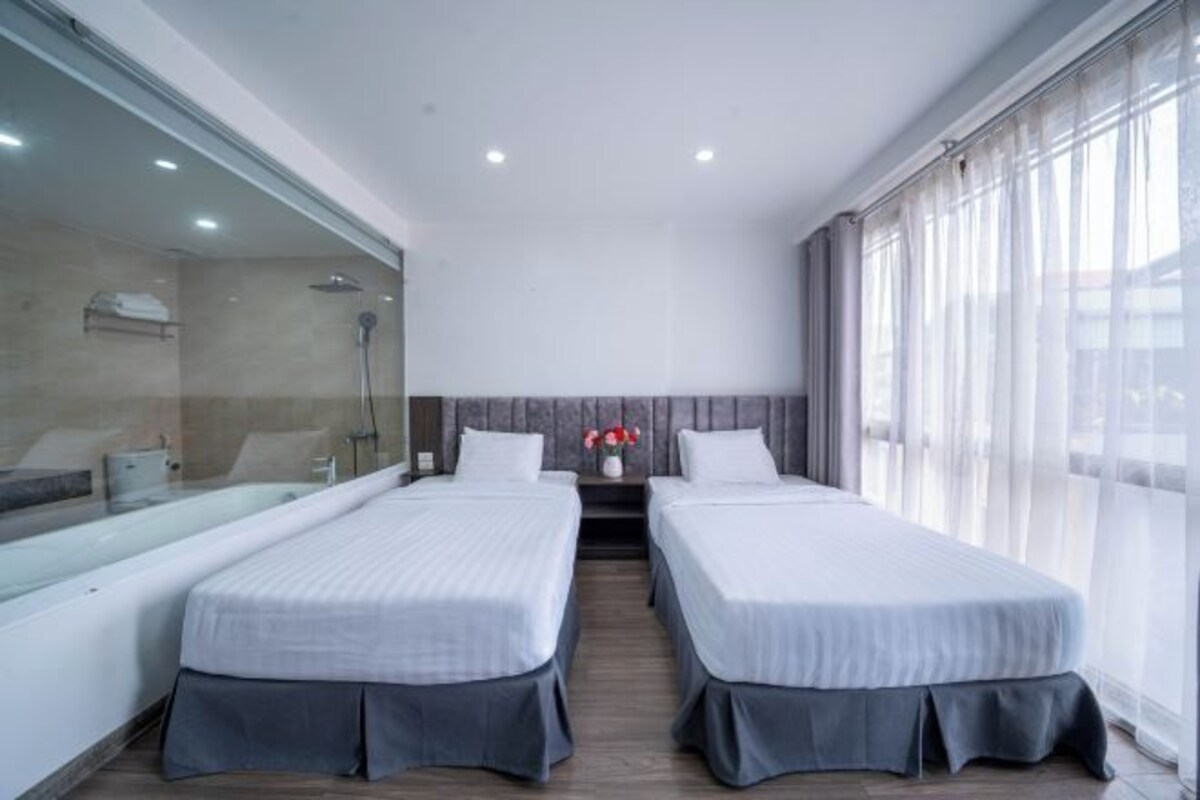 Habitación de hotel con dos camas, un ventanal grande y zona de ducha.
