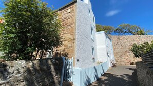 Ein Steinhaus mit weißer Fassade, einem kleinen Balkon mit Blumen und einem Baum im Vordergrund.