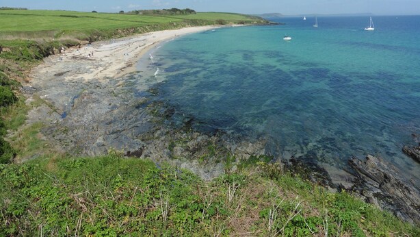 Paisagem costeira com praia arenosa, águas azuis cristalinas e barcos ao longe.