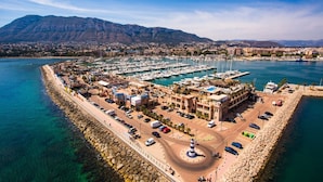 A coastal marina with boats docked, a lighthouse, and a rocky breakwater. - 111 Alberca 8-3 (Denia)