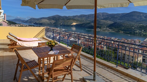 Une terrasse avec une table, des chaises et un parasol, d’où l’on a vue sur un lac et des montagnes.