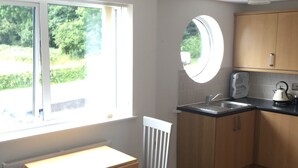 Een kleine keuken met raam, een ronde spiegel en een eethoekje met tafel en stoelen.