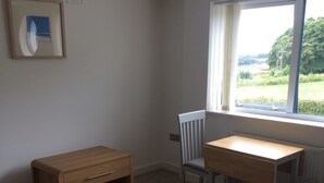 Een kamer met een bank, een houten tafel en een stoel. Er is een raam met uitzicht op groen.