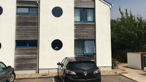 Een modern gebouw met een parkeerplaats, met een auto en een gebouw met ronde ramen en een schuin dak.
