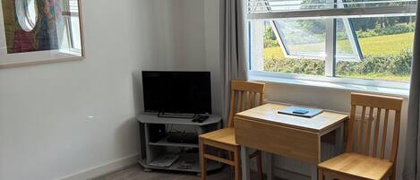 Un salon moderne avec un téléviseur à écran plat, une table à manger en bois et des chaises. Un canapé est visible au premier plan.