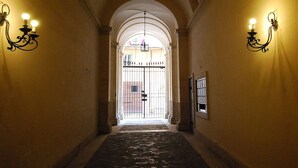 A corridor with an arched ceiling, a stone floor, and wall-mounted lighting fixtures.
