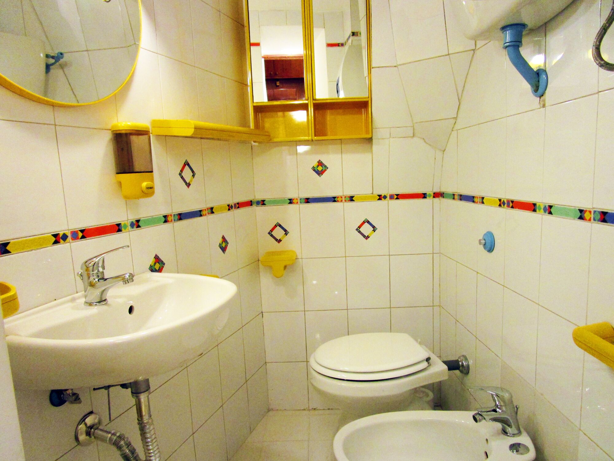 A bathroom with a sink, toilet, and bidet, tiled with a geometric pattern.