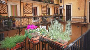 A courtyard with a balcony, potted plants, and a building with multiple windows and doors.