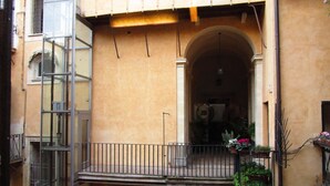 A building with a balcony, a staircase, and an archway leading to an interior space.