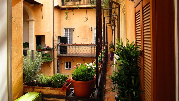 A narrow courtyard with balconies, potted plants, and a small table.