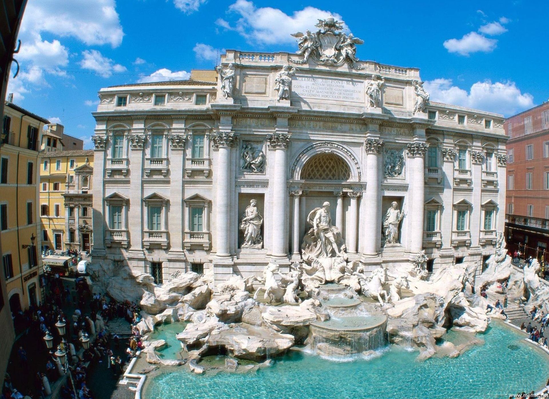 Un imposant bâtiment à l’architecture classique, une grande fontaine et un ciel d’un bleu limpide.