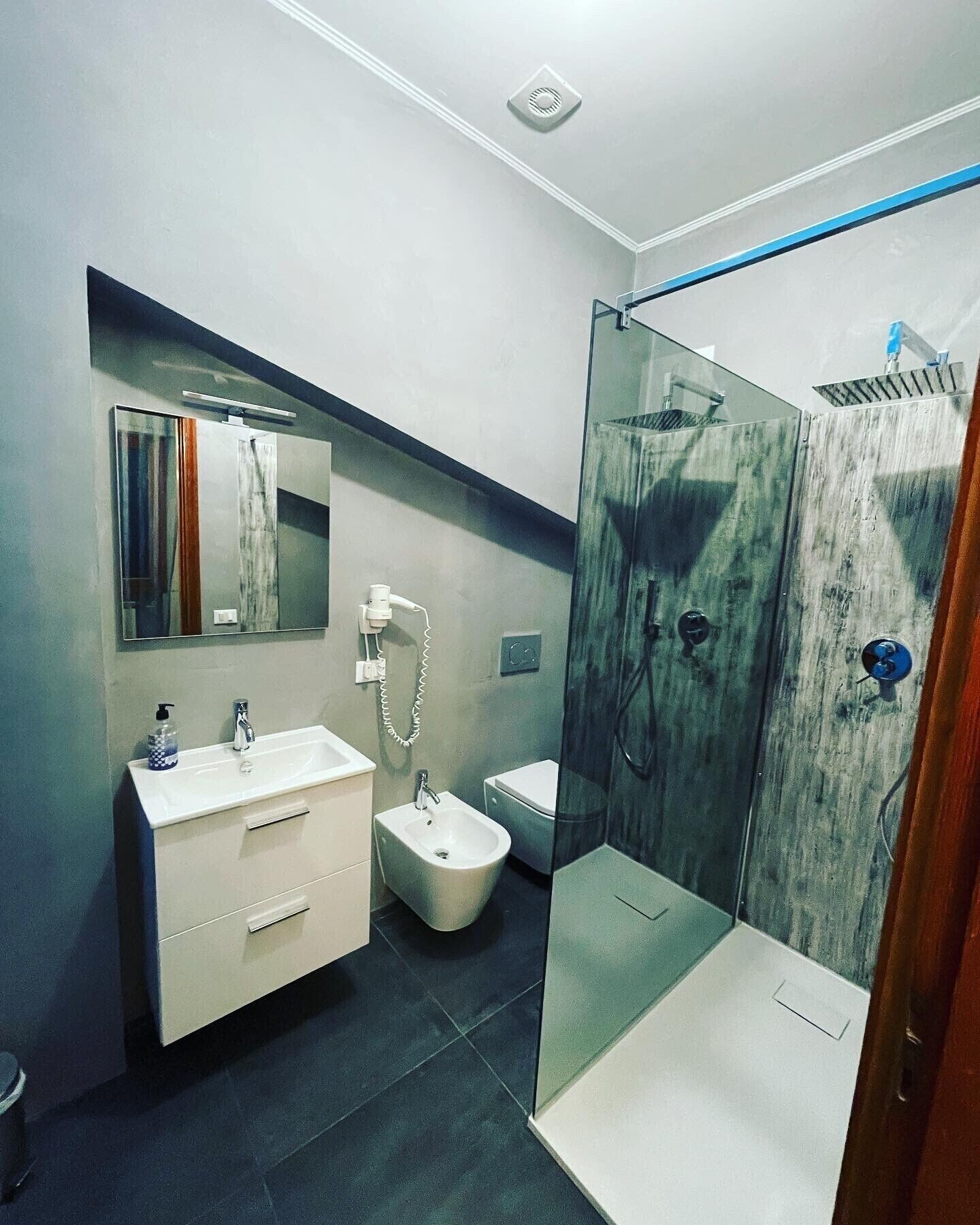 Un baño moderno con ducha de vidrio, tocador con espejo, bidé y retrete.