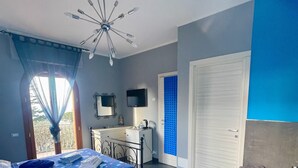 Een slaapkamer met een bed, een bureau, een stoel, een televisie, een plafondventilator en een badkamer met een bad.
