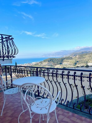 Ein Balkon mit Tisch und Stühlen, der auf eine Küstenlandschaft mit blauem Himmel blickt.