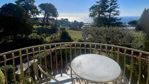 Een balkon met een tafel en stoelen, met uitzicht op een fraai landschap van bomen en een verder gelegen waterpartij.