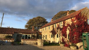 A stone building with a tiled roof, a green telephone booth, and a garden area with outdoor seating. - Bilsdale Cottage, a dog friendly hidden gem near Helmsley and the North York Moors National Park (Sproxton, York)