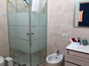 A bathroom with a glass-enclosed shower, a bidet, a sink, and a mirror with a decorative frame. - A Perfect Starting Point for Coastal Exploration for family or friends. (Santa Margherita di Pula)